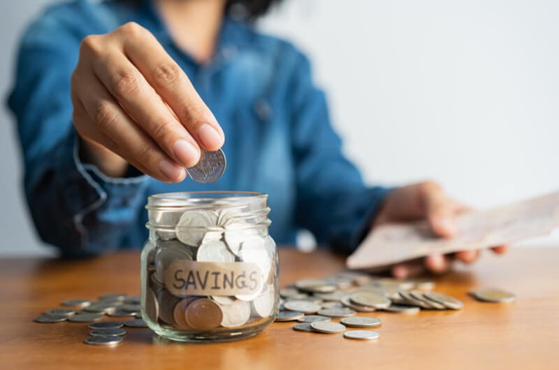 woman hand puts coins in jar - top tips for saving on a limited budget planning services farmington
